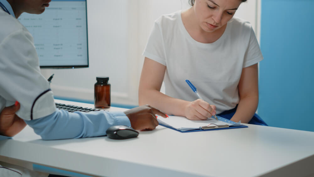 Patient reviewing embryo storage consent forms with a pen on a clinic desk.